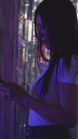 Vertical-Video-Of-Woman-Checking-Messages-On-Mobile-Phone-In-Nightclub-Or-Funfair